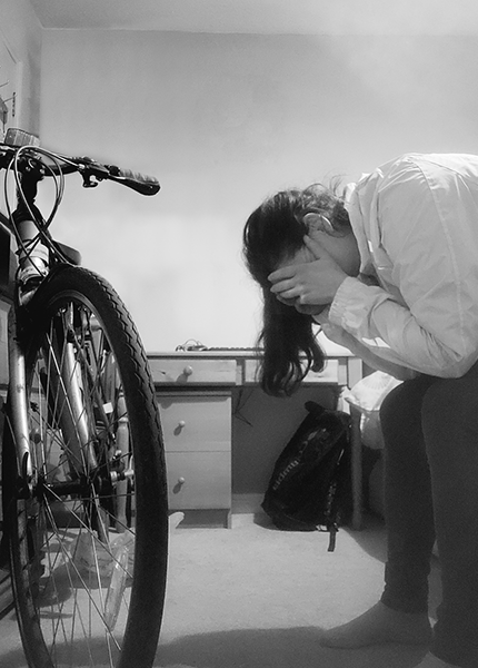 A woman sits on a bed with her head in her hands and a bike in front of her A woman sits on a bed with her head in her hands and a bike in front of her
