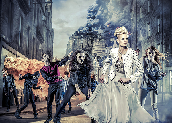 A dressed up woman runs down a street chased by zombie-like people with fire in the background A dressed up woman runs down a street chased by zombie-like people with fire in the background