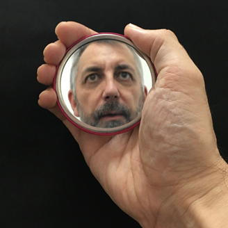 A hand holding a small mirror with the reflection of a man in it A hand holding a small mirror with the reflection of a man in it
