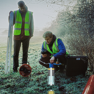 A researcher crouching on the grass testing the ground with a researcher standing watching A researcher crouching on the grass testing the ground with a researcher standing watching