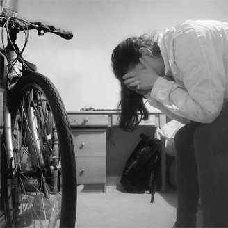 A woman sits on a bed with her head in her hands and a bike in front of her A woman sits on a bed with her head in her hands and a bike in front of her