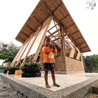 A child stands in front of a bamboo building A child stands in front of a bamboo building