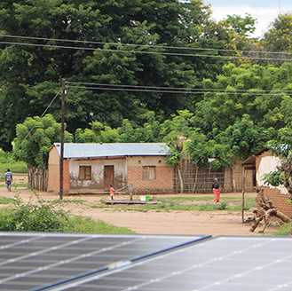 Solar panels in the foreground, small buildings with rooftop solar panels in the background, in Malawi Solar panels in the foreground, small buildings with rooftop solar panels in the background, in Malawi