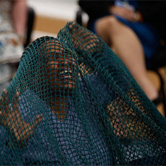 An African woman kneels with hands in the air as if in pain, covered with a large blue fishing net, surrounded by an audience An African woman kneels with hands in the air as if in pain, covered with a large blue fishing net, surrounded by an audience