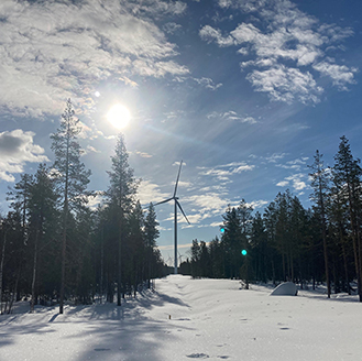 A snowy landscape with tall pine trees lining the horizon and a wind turbine in the middle. The sun low in the sky just above. A snowy landscape with tall pine trees lining the horizon and a wind turbine in the middle. The sun low in the sky just above.