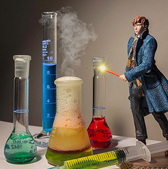 A figurine of a man with a wand stands to the right of various beakers filled with colourful liquids with smoked emerging, and a syringe and tablets in the foreground. A figurine of a man with a wand stands to the right of various beakers filled with colourful liquids with smoked emerging, and a syringe and tablets in the foreground.