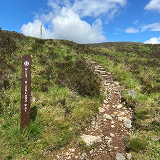 A rocky pathway leading up a grassy hill, with a sign saying the West Highland Way on the left A rocky pathway leading up a grassy hill, with a sign saying the West Highland Way on the left