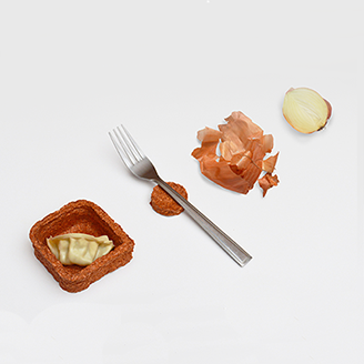 A slice of onion next to crumpled onion skins, a fork next to a little rough-textured container holding a gyoza A slice of onion next to crumpled onion skins, a fork next to a little rough-textured container holding a gyoza