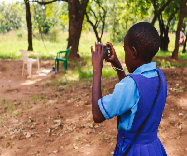 School pupil with back to camera taking photograph of environment