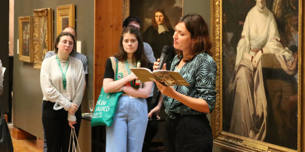 A woman reads a poem to an audience in an art gallery A woman reads a poem to an audience in an art gallery