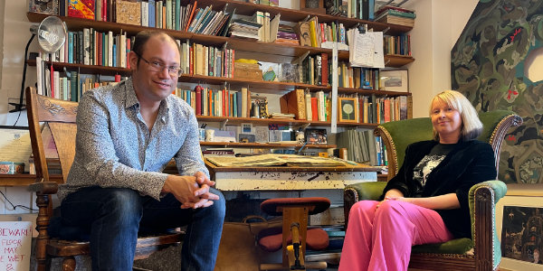 A man and a woman sitting in front of a library of books A man and a woman sitting in front of a library of books