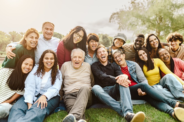 Group of young and older adults sitting together on grass outside Group of young and older adults sitting together on grass outside
