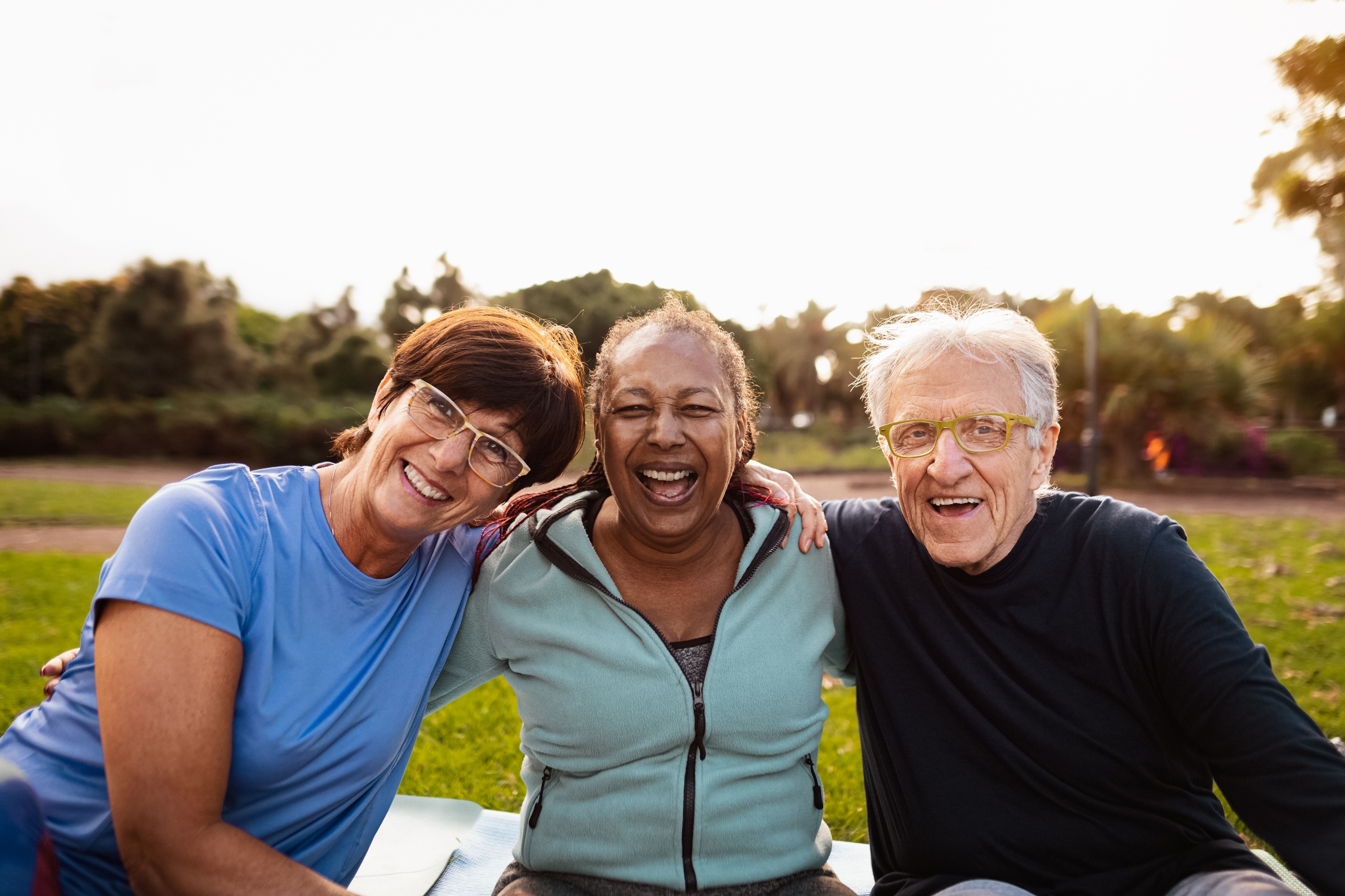 Two older females and an older male sitting together on grass outside. Two older females and an older male sitting together on grass outside.