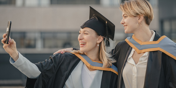 Two graduates taking a picture of themselves on a mobile phone Two graduates taking a picture of themselves on a mobile phone