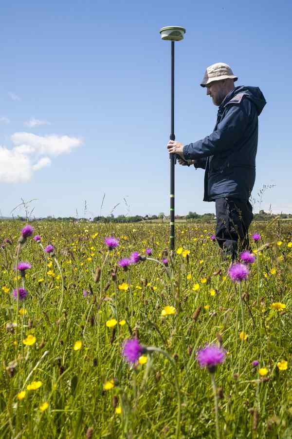 A person standing in a green field holding a tall measuring devide A person standing in a green field holding a tall measuring devide