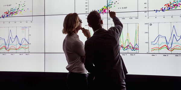 Business men in a dark room standing in front of a large data display Business men in a dark room standing in front of a large data display