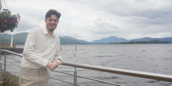 Duncan leaning against a railing overlooking a loch with hills in the distance